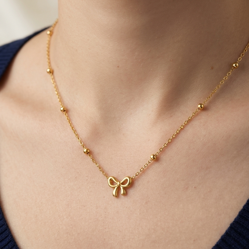 Gold necklace with a bow pendant on a person wearing a blue top.