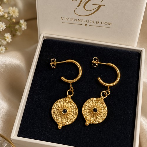 A pair of gold hoop earrings with textured circular dangles and small black center stones, presented in a white jewelry box with a black velvet insert. The inside lid shows the brand name 'Vivienne Gold'.