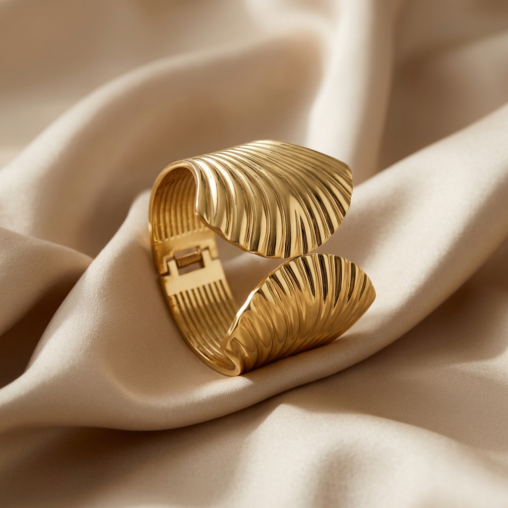 A wide gold cuff bracelet with a textured, ribbed leaf-like design and a spring-ring clasp, shown on a white background.