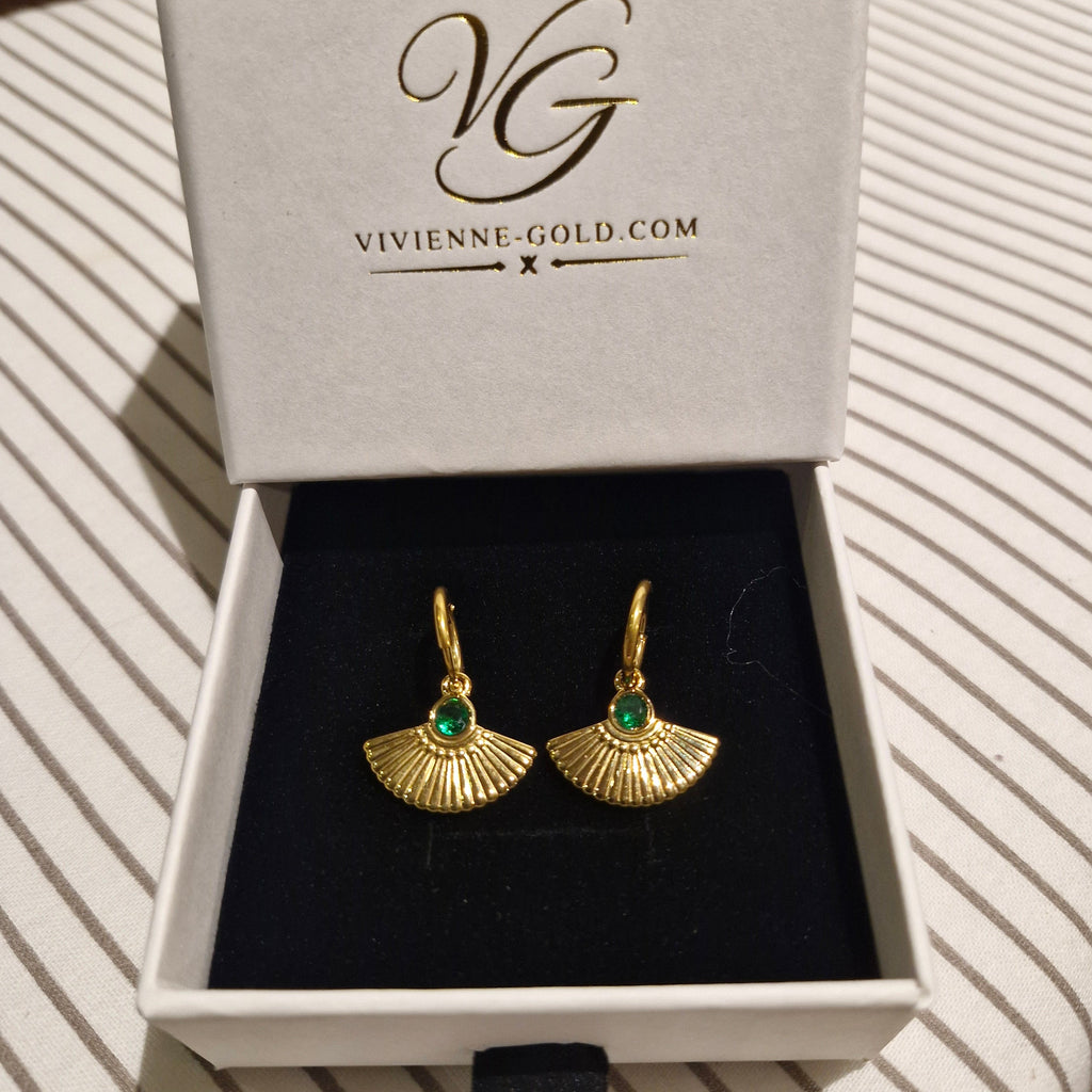 A pair of gold fan-shaped drop earrings with small green stone centers, presented in an open white jewelry box with the brand name VIVIENNE-GOLD.COM printed inside the lid, set on a striped fabric surface.