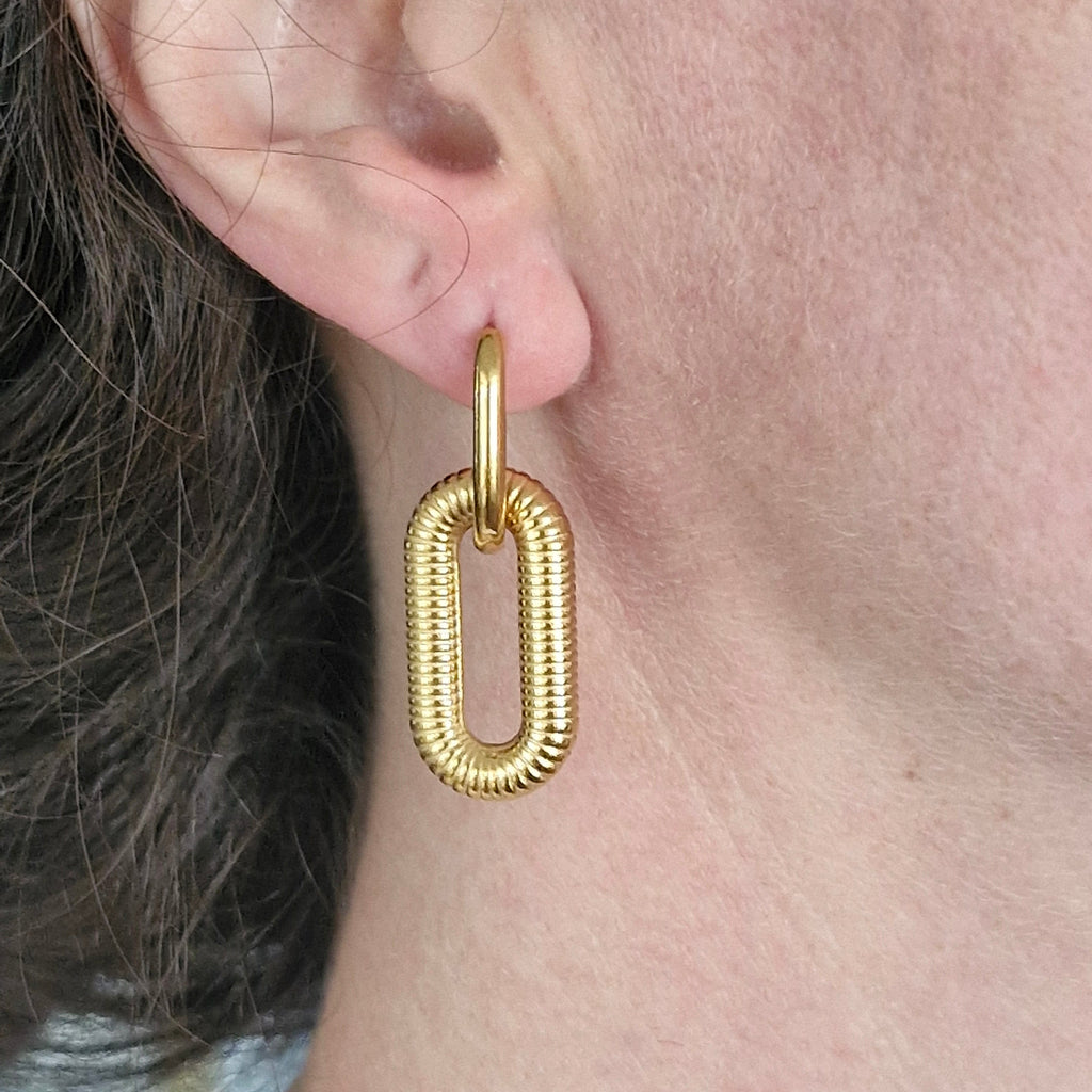 A close-up of a person's ear wearing a textured waterproof, stainless steel, 18k Gold PVD  drop earring with a rounded, snake-like ribbed design.