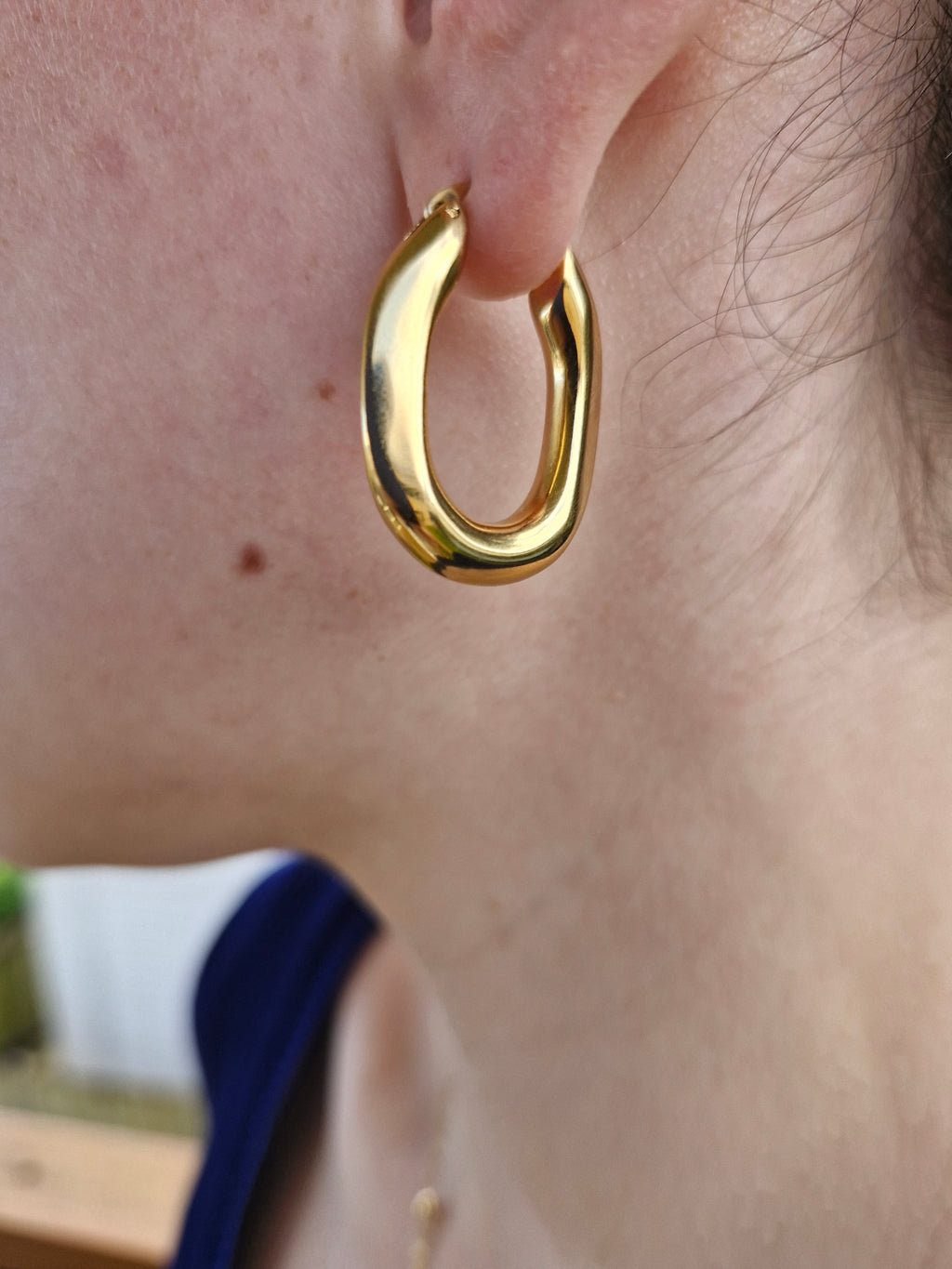 A close-up of a person wearing a polished gold huggie hoop earring.