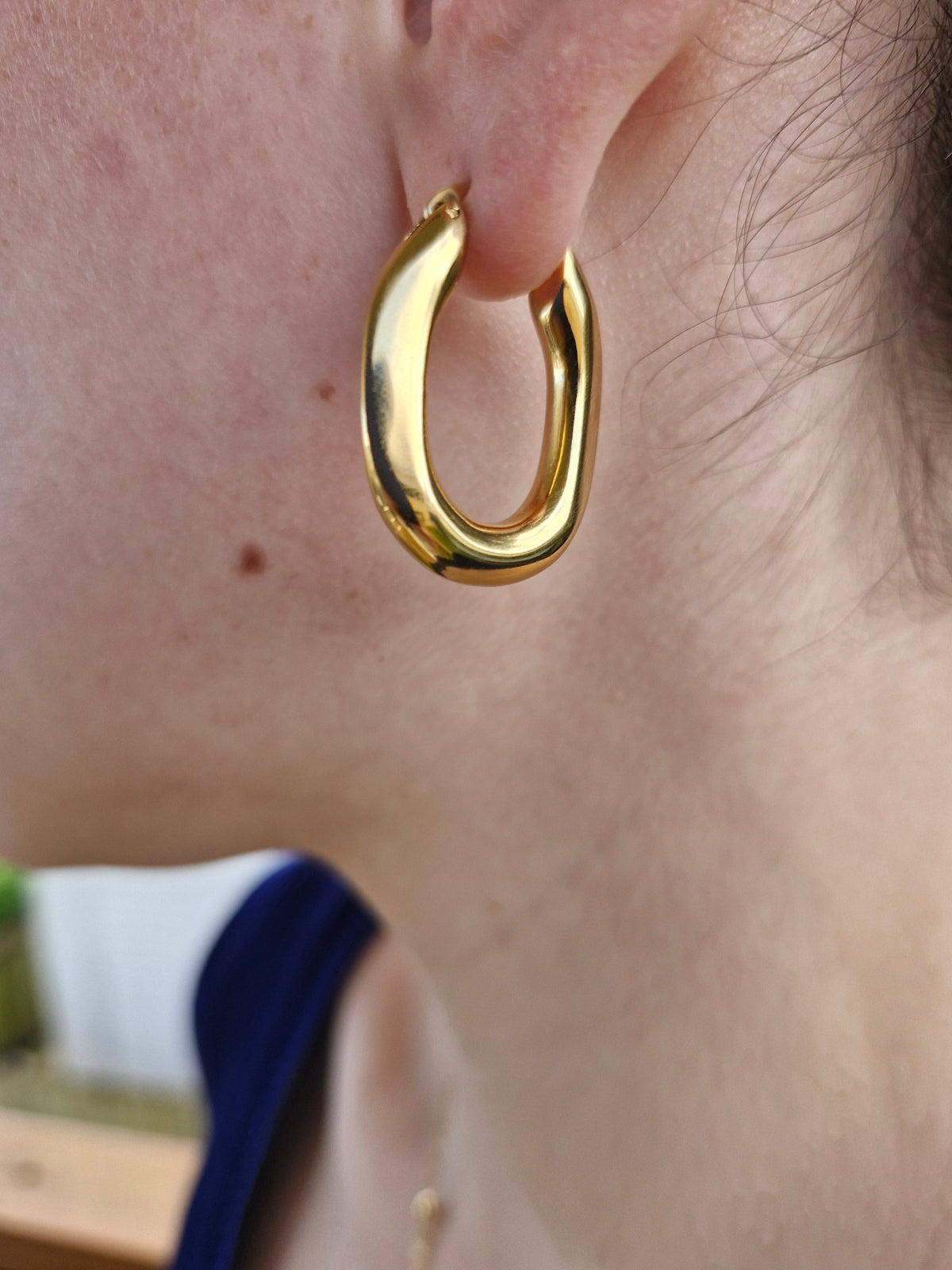 A close-up of a person wearing a polished gold huggie hoop earring.