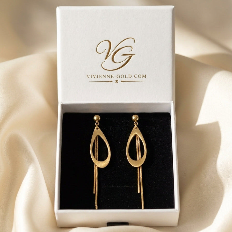 A pair of gold teardrop-shaped drop earrings displayed inside an open white jewelry box with a black velvet insert. The inside lid of the box shows the brand name 'Vivienne Gold' in gold lettering.