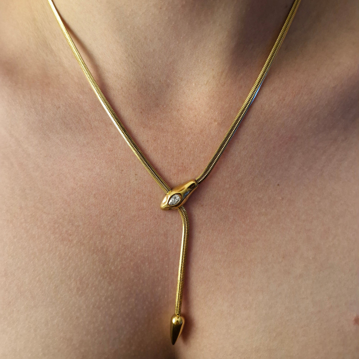 A close-up of a person's chest wearing a delicate gold chain back strap with a small clear stone accent at the center.