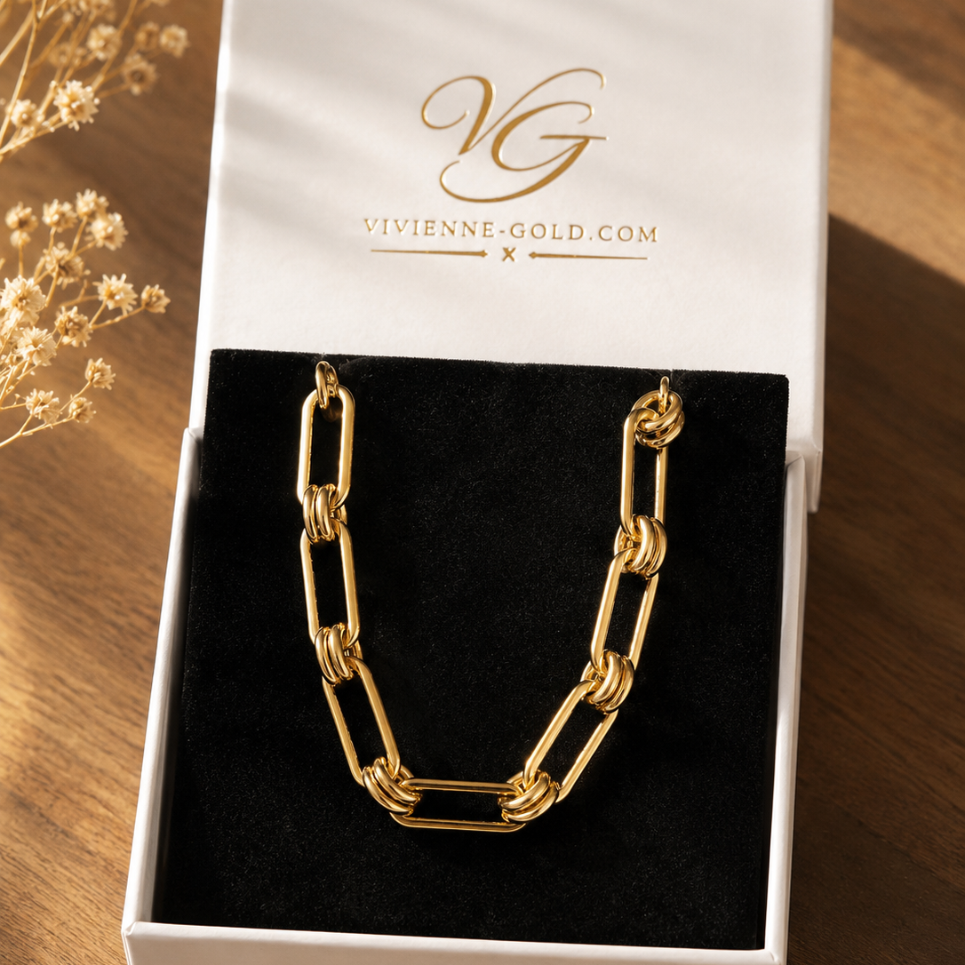 Gold chain necklace in a Vivienne Gold box on a wooden surface with dried flowers.